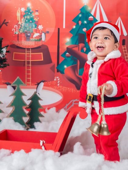 A joyful little Santa, laughing as he stands by his sleigh full of jingle bells.