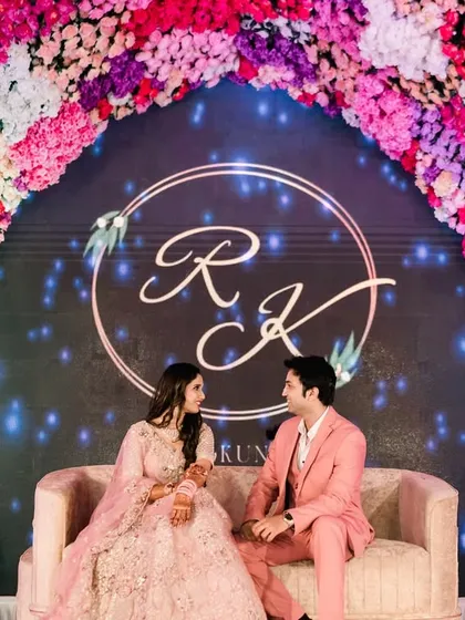 Seated against a backdrop of their elegant monogram and a stunning floral arch, the couple shares a quiet moment. This shot showcases the personalized details and grand scale of a modern engagement stage.