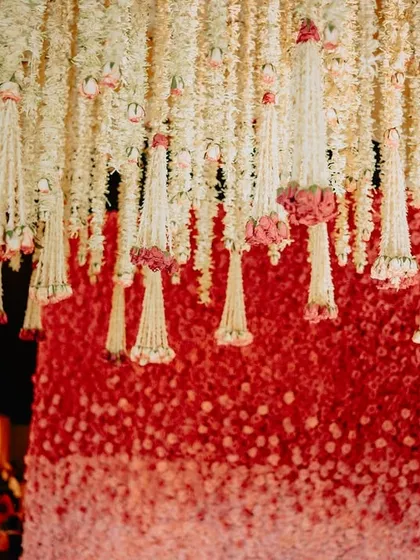 A close-up of the floral backdrop, showing the gradient of red and pink roses, with strings of white jasmine flowers hanging in front for a delicate, layered effect.