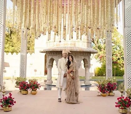 The couple stands at their mandap, framed by hanging floral strings and the architectural beauty of the venue. This setup shows how minimalism can be incredibly impactful and elegant.
