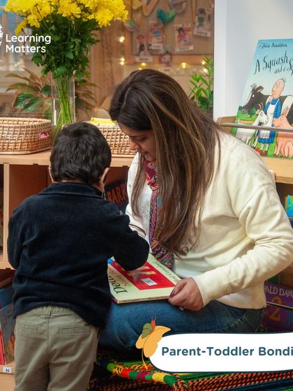 A quiet moment of connection between a parent and child over a book. Our Parent-Toddler programs are designed to foster these bonds, providing a supportive space for families to learn and play together.