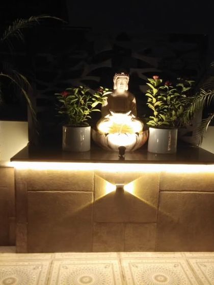 A Buddha water feature at night. The combination of the statue, the flowing water, and the warm lighting creates a peaceful and meditative focal point.