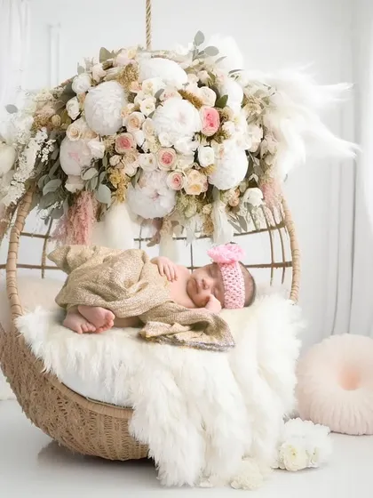 A beautiful boho-chic setup with a newborn sleeping in a hanging wicker chair decorated with pampas grass and flowers.