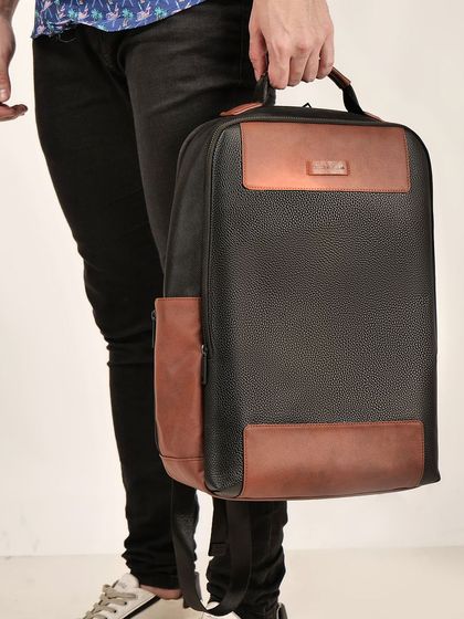 A model holding a black and brown leather backpack, demonstrating its size and how it's carried.