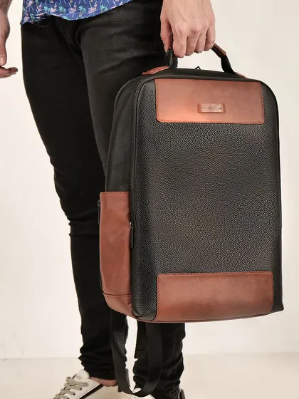 A man holding a black and brown leather backpack. This shot gives a sense of the bag's scale and how it's carried, focusing on its materials and design.