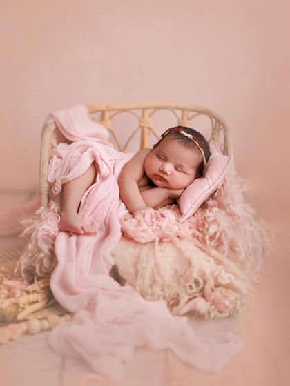 Wrapped in rosy hues. This unswaddled pose on a miniature bed draped with soft pink fabric shows off the baby's tiny features in a beautiful, relaxed way.