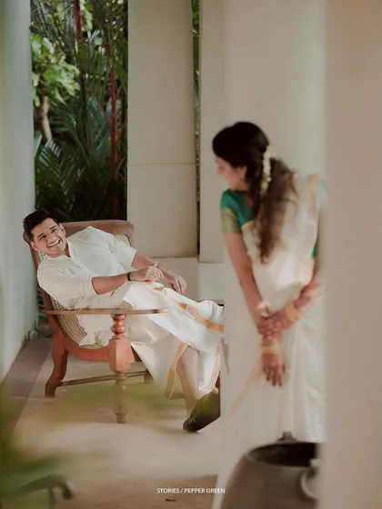 A candid moment of the groom relaxing in a chair while his bride looks on with a shy smile.