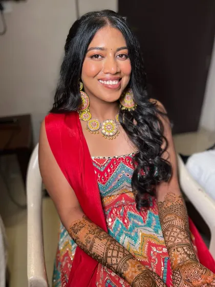 A smiling bride at her Mehendi. The makeup is designed to be long-lasting and comfortable for the hours-long henna application.