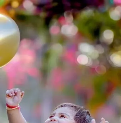 A baby's joyful expression as they reach for a golden balloon. This shot, with its colorful bokeh background, is full of wonder and happiness.