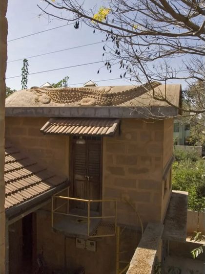 A unique detail from the Professor's Residence: a crocodile sculpture made of mud mortar crawling over a vaulted roof. This playful element was created by artist Sanjay Singh, integrating art directly into the architecture.
