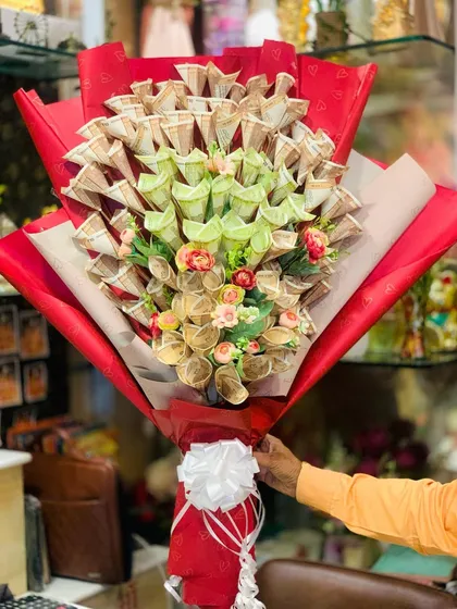 A view of the currency bouquet being held, showing its impressive size. The red wrapping paper provides a striking contrast to the green and beige notes.