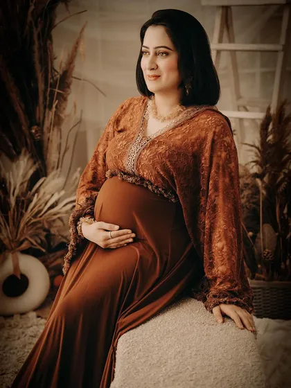 A classic seated portrait in our warm, earthy-toned boho studio. The rich colors of the gown and the rustic props create a comfortable and beautifully styled scene.
