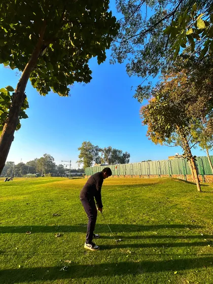 A golfer practices his chipping under a clear blue sky, with the bunker visible in the background.