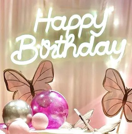 Another close-up of a 'Happy Birthday' neon sign, this time paired with delicate butterfly decorations for a whimsical feel.