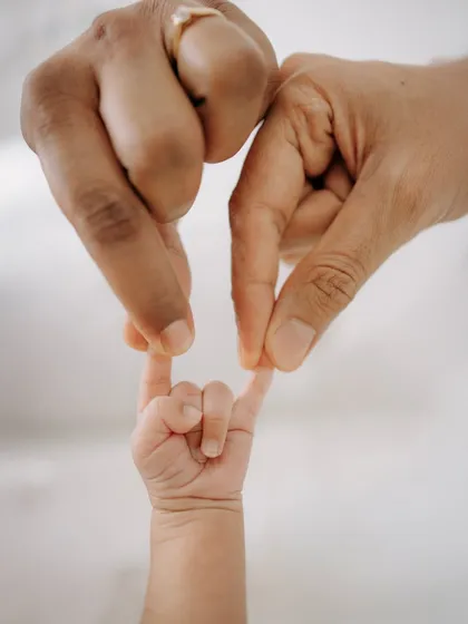 A creative pose with the baby's tiny hand reaching up to meet their parents' fingers.