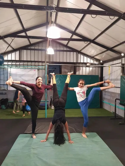 A creative three-person pose combining a handstand with standing leg-hold stretches. This shows how we mix gymnastics and flexibility training.