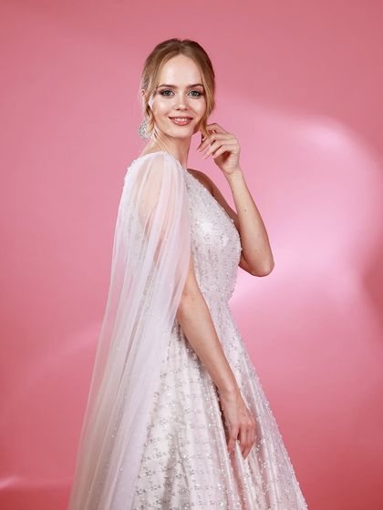 A side-profile portrait of Irina Rudakova in her white gown, with a sheer cape creating a sense of movement and grace.