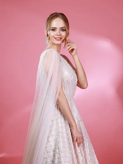 A side-profile portrait of Irina Rudakova in her white gown, with a sheer cape creating a sense of movement and grace.