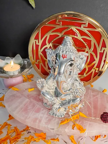 A truly mesmerizing piece, this silver Ganesha idol is set against a striking red and gold geometric backdrop. The polished rose quartz base enhances its beauty, creating a perfect harmony of color, material, and spiritual significance.