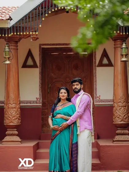 A classic portrait of a couple in front of a traditional house, showcasing their coordinated ethnic outfits.