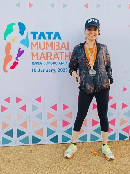 Posing by the Tata Mumbai Marathon banner, Dr. Indu Tandon showcases her finisher's medal. Her journey as a doctor, mother, and national-level athlete is an inspiration to our community.