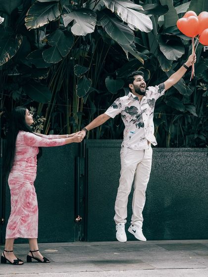 A fun, high-energy shot of the groom jumping for joy while holding heart-shaped balloons, as the bride holds him back.