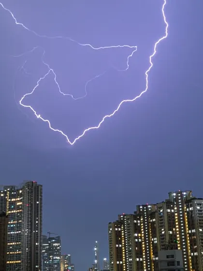 A massive fork of lightning strikes downwards, perfectly framed between the tall buildings of Mumbai at night.