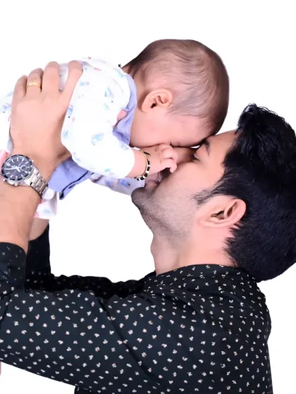 A father lovingly kissing his baby's forehead while holding them up in the air.