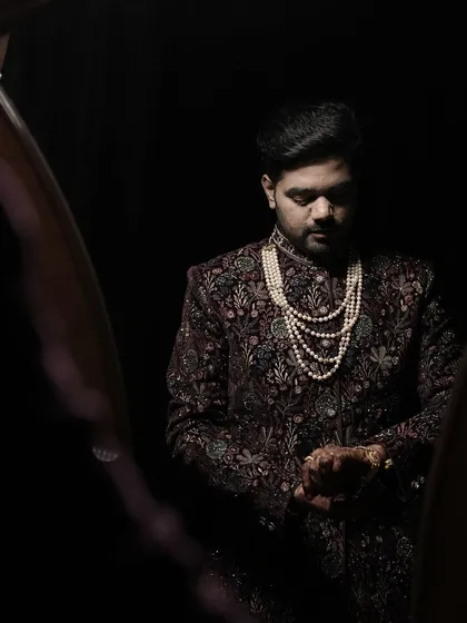 A classic portrait of the groom in a beautifully embroidered sherwani and pearl necklace, checking his watch as he prepares for the ceremony.