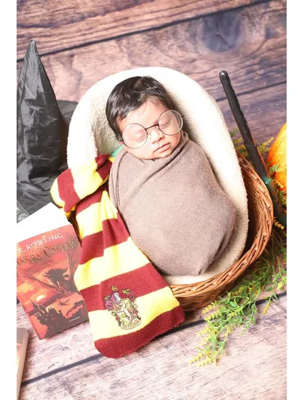 The magic is real with our Harry Potter inspired newborn shoot. Your little one becomes the newest student at Hogwarts, complete with a Gryffindor scarf, round glasses, and a magic wand, all set for a fantastical journey.