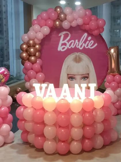 A fabulous Barbie-themed party for Vaani's first birthday, featuring a round backdrop, a balloon-covered cake table, and marquee letters.
