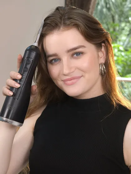 A close-up of a model holding a black water flosser. The focus on the user's happy expression helps to sell the benefits of the product, not just its features.