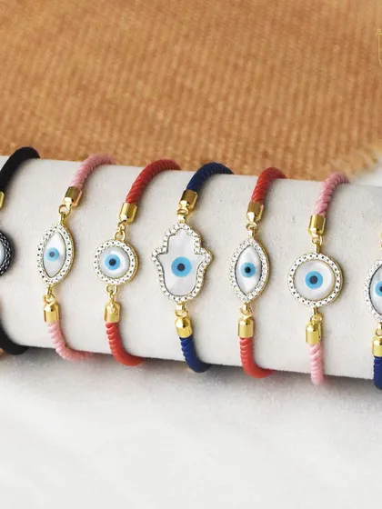 Tie the bond of love and protection with my evil eye rakhis. This image shows a variety of thread bracelets with different evil eye and hamsa designs.