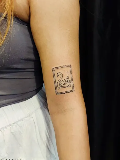 A unique postage stamp tattoo featuring a swan. This creative, fine-line design is a nod to travel and elegance, framed in a classic stamp border.