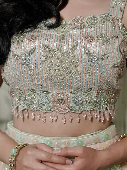 A close-up of the intricately embroidered blouse of the pastel lehenga, showing the mix of peach, green, and silver threadwork.