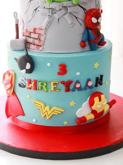 A close-up of the lower tier of the superhero cake, showcasing the colorful logos of Iron Man, Wonder Woman, and Batman.