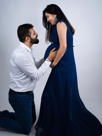 A moment of pure joy and anticipation. The dad-to-be kneels to listen to the baby bump, looking up at his partner with a huge smile.