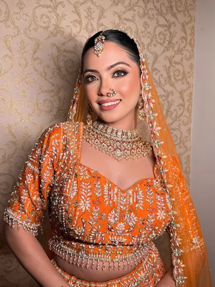 A happy bride glowing in her orange lehenga. The makeup is radiant and fresh, letting her joyful smile be the centerpiece.