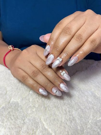 A delicate and shimmery set of almond-shaped extensions with a pearly white finish and small, sparkling silver bow charms.