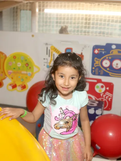 This little unicorn fan is all smiles as she peeks out from behind a yellow slide in the toddler area.