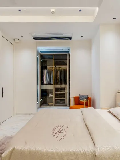 A view from the side of the bed, highlighting the seamless integration of the walk-in closet. The curved wall and minimalist design contribute to the room's open and airy feel.