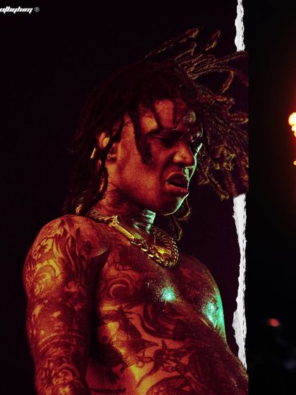 An intense close-up of Swae Lee performing at Rolling Loud, with dramatic red lighting highlighting his intricate tattoos and raw emotion.