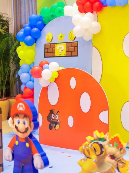 A detailed shot of the Super Mario backdrop, featuring Mario, a Goomba, and Bowser Jr. The colorful balloon arch and mushroom prop complete the immersive scene.