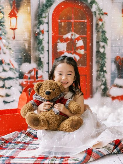 A little girl hugging her teddy bear in a magical, snowy Christmas scene.