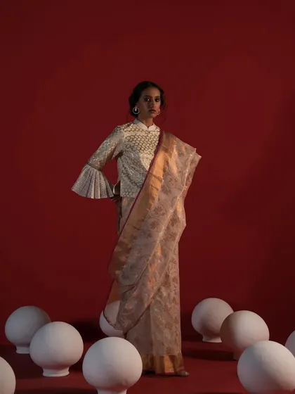 A model stands in a studio setting wearing a handwoven saree with a unique bell-sleeved blouse, showcasing a modern twist on traditional wear.