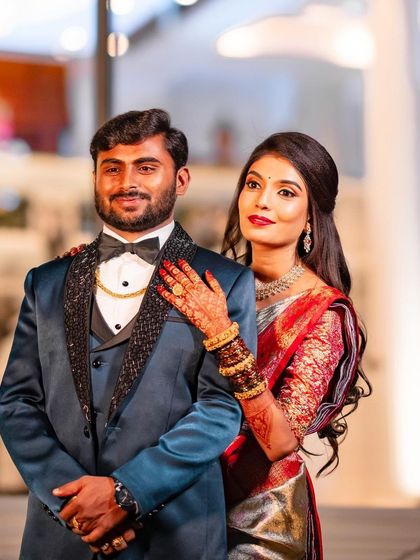 A classic couple portrait from the reception. The bride's makeup is elegant and polished, with a bold red lip that stands out beautifully against her metallic-sheen saree.