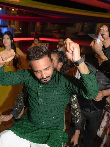 The groom letting loose on the dance floor during a pre-wedding celebration like Mehendi or Sangeet, surrounded by friends and family.
