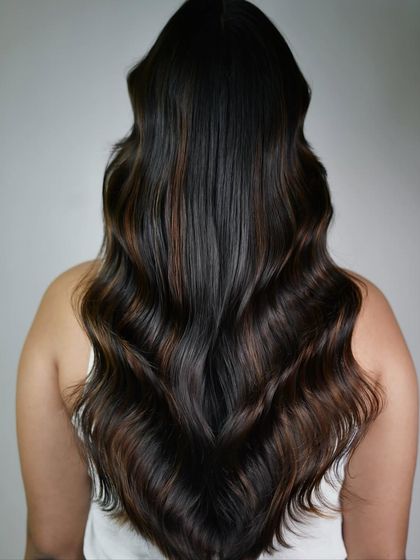 A full view of the cinnamon balayage from the back. The placement of the lighter pieces creates a cascade of color that looks stunning on long, wavy hair.
