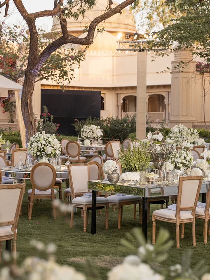 The outdoor dining arrangement for the 'Sheesh Mahal' reception, set amidst the lush gardens of The Oberoi Udaivilas.