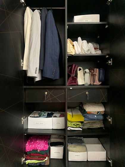 This wardrobe combines hanging space for suits and blazers with shelf storage for folded clothes, bags, and other items, all within a sleek, dark finish.